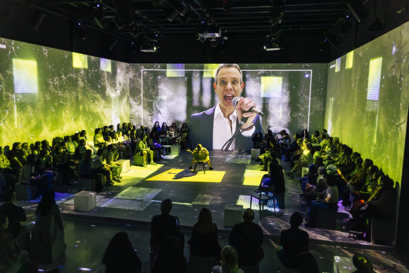 The immersive staging of Next to Normal — the audience surrounds the stage beneath a vast projection of the lead performer. Photo by Chaskielberg.